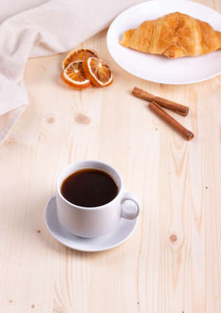 a white ceramic cup with black espresso, french croissant as breakfast or snack concept on rustic, natural texture wooden surfaceの写真素材