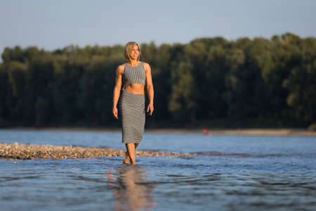 Athletic girl in striped dress walking at a riverの写真素材