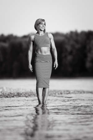 Athletic woman in striped dress walking at a riverの写真素材