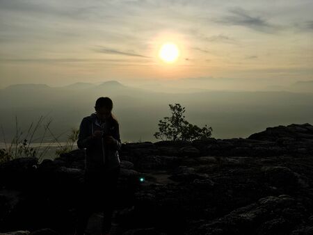 Silhouette scene of woman standing on the cliff mountain, sunset backgroundの写真素材