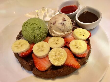 Waffles topped with ice cream, banana, strawberry and strawberry chocolate sauceの写真素材