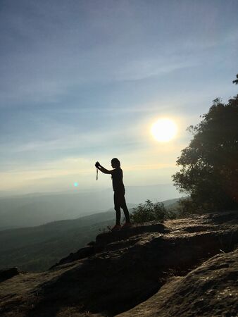 Silhouette of woman taking photo with smartphone at mountain peak on sunlight sceneの写真素材