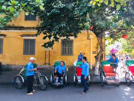 Local tricycle and driver at Hoi An ancient town street, Vietnam. yellow building backgroundの写真素材
