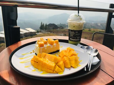 Mango cheesecake with fresh mango and matcha frappe drink, enjoy dessert order on mountain view background.の写真素材