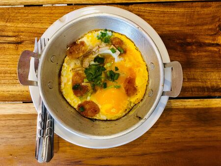 Homemade breakfast fried egg in a pan with sausage and topping on wooden background, top viewの写真素材