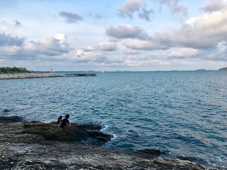 Scenery of sea beach with people seating relax feel on reef coast and blue sky clouds backgroundの写真素材