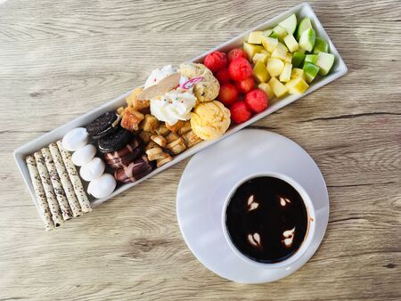 Chocolate fondue sauce dipped with fruits and confectionary snack on wooden background, top viewの写真素材