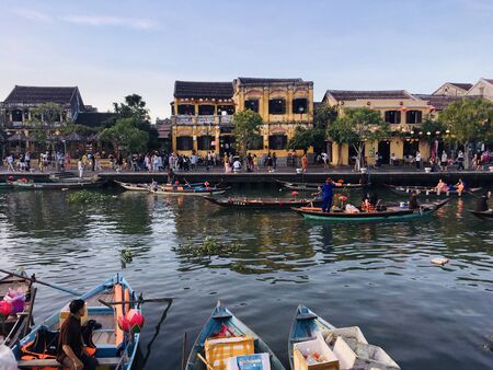 Scenery view of mustard yellow building style with crowd traveler and traditional boat on river at Hoi an ancient town, Vietnamの写真素材