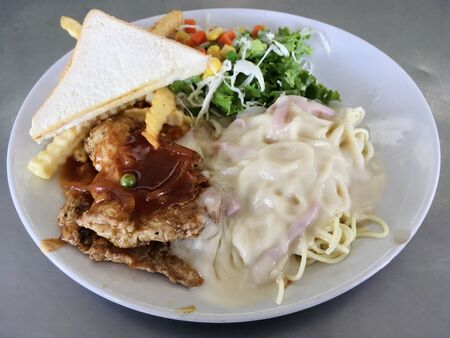 Pork steak and spaghetti carbonara topping with vegetable salad and bread toastの写真素材