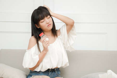Exhausted asian female suffer from headache ready to have painkiller to ease symptoms.の写真素材