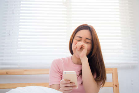 Young Asian woman look at the smart phone and laugh on a bed.の写真素材