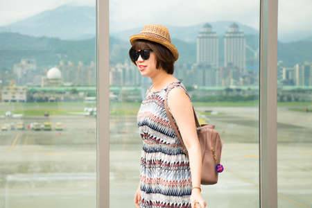 Young asian woman goes at airport at window with a suitcase waiting for plane.の写真素材
