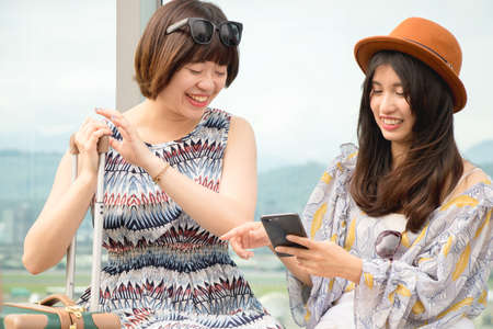 Two asian women using app on mobile phone, looking at screen of smart phone, texting, watching...