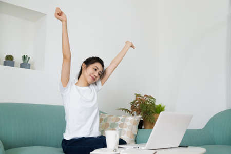 Happy relaxing woman stretching in front of computer at home. Smiling female reach out, put hands up sitting at laptop. People at work, remote work, studying, working online conceptの写真素材