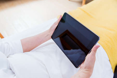 Closeup of senior woman's hand using tablet in the bed at home. Photo without face.