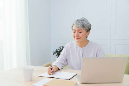 Senior Asia woman is working from home, using laptop and smart phone.の写真素材