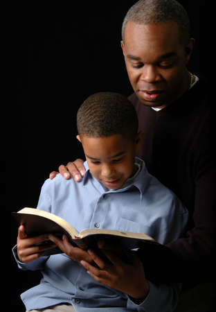 Father and son reading a Bible over a black background.の写真素材