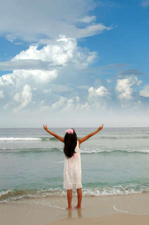 Girl with dress and ribbon with arms wide open expressing joy and freedom in fornt of the waterの写真素材