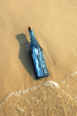 Message in a vintage blue bottle on a sandy shoreの写真素材