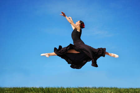 Ballerina dressed in black jumping high over a blue sky.