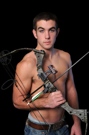 Portrait of young man with bow and arrow isolated over a black background.の写真素材