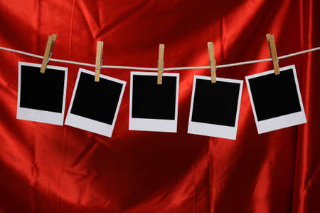 Blank Polaroid photos hanging by a clothespin over a red satin background