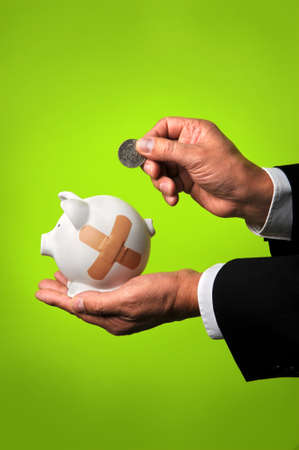 Businessman saving coing in piggy bank with bandagesの写真素材