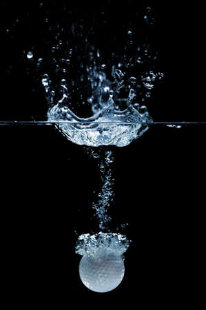 Golf ball splashing into water isolated over a black backgroundの写真素材