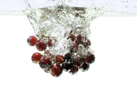 Red grapes splashing into water over a white backgroundの写真素材