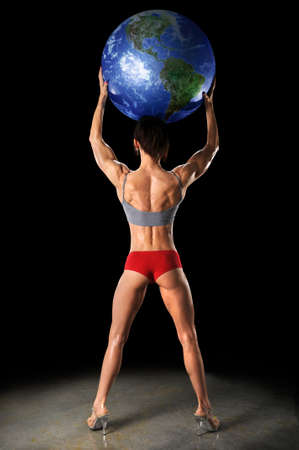 Female bodybuilder lifting earth over dark backgroundの写真素材
