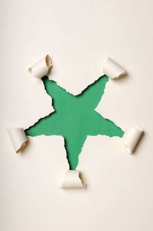 Old discolored paper ripped to form star over green backgroundの写真素材