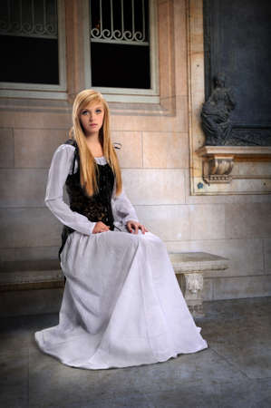 Beautiful young Woman dressed in Renaissance clothing sitting on benchの写真素材