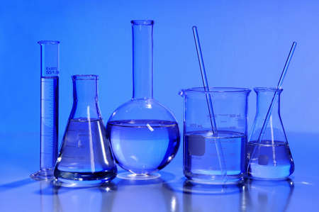 Laboratory glassware in blue light over reflective tableの写真素材