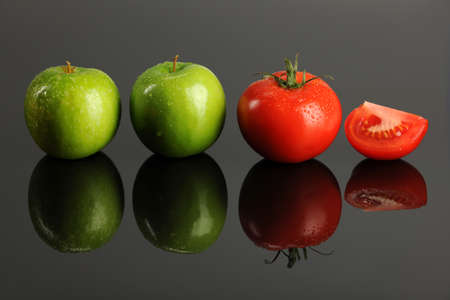 Green apples and tomatoes over reflective surfaceの写真素材