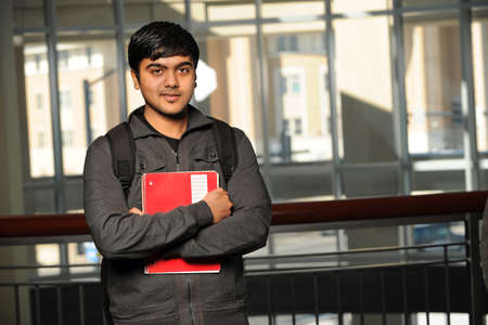 Portrait of young Indian student with school backpack holding notebook inside school building