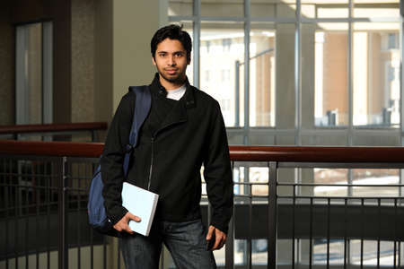 Portrait of young Indian student holding book inside building