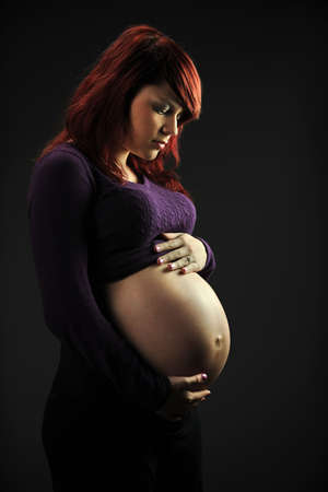 Portrait of beautiful young pregnant woman in profile view over dark backgroundの写真素材