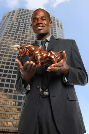 African American businessman holding bull with office building in backgroundの写真素材