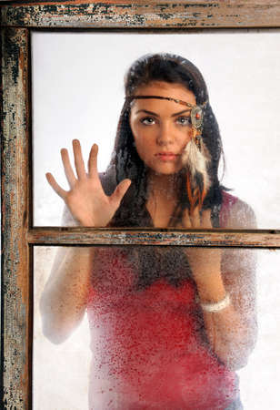 Portrait of beautiful young woman wearing feather headband looking through old window