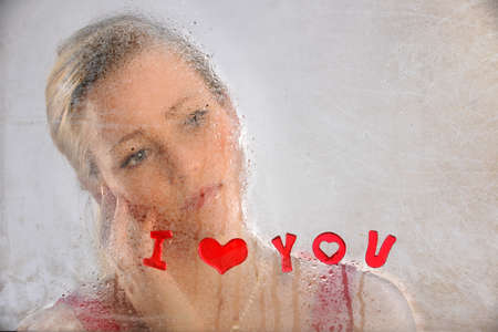 Beautiful young woman looking out grungy window with I Love You text