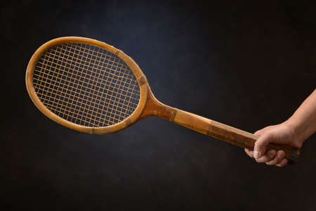 Man's hand holding vintage tennis racket over dark backgroundの写真素材