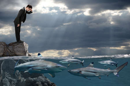 Competitive busines concept with businessman looking at sharks swimming in oceanの写真素材