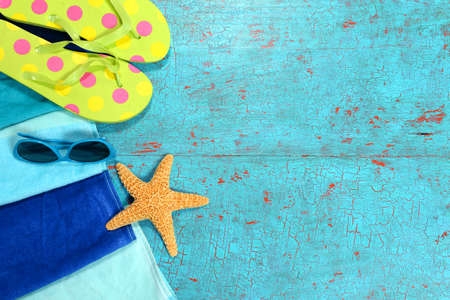 Beach towel, sunglasses, starfish and flip flops over painted wood planksの写真素材