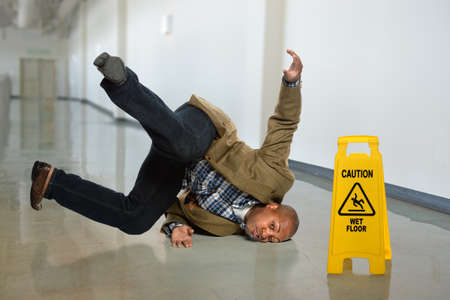 African American businessman falling on wet floor in officeの写真素材