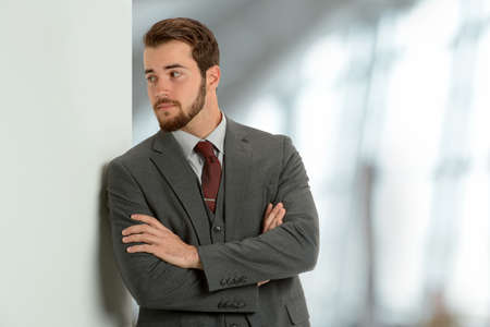 Portrait of young businessman leaning on wall inside office buildingの写真素材