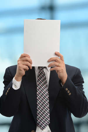 Businessman hiding behind papers inside office buildingの写真素材