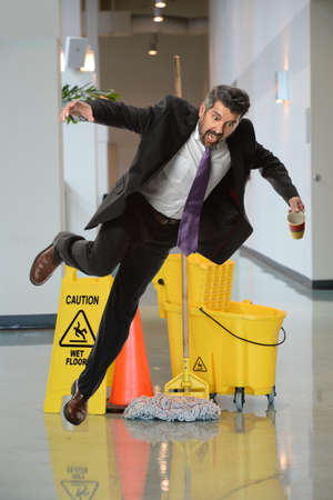 Businessman falling on wet floor inside office buildingの写真素材