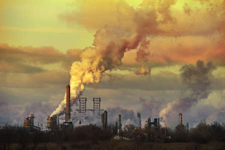 Oil refinery at sunset spewing gases from smoke stacksのeditorial素材