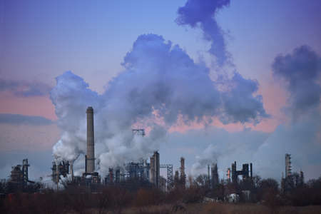 Flock of birds flying by oil refinery smoke stacksのeditorial素材