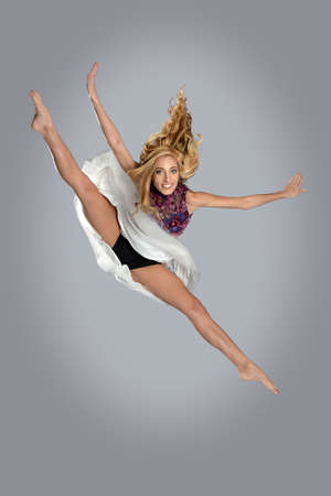 Young woman jumping and doing splits over gray backgroundの写真素材